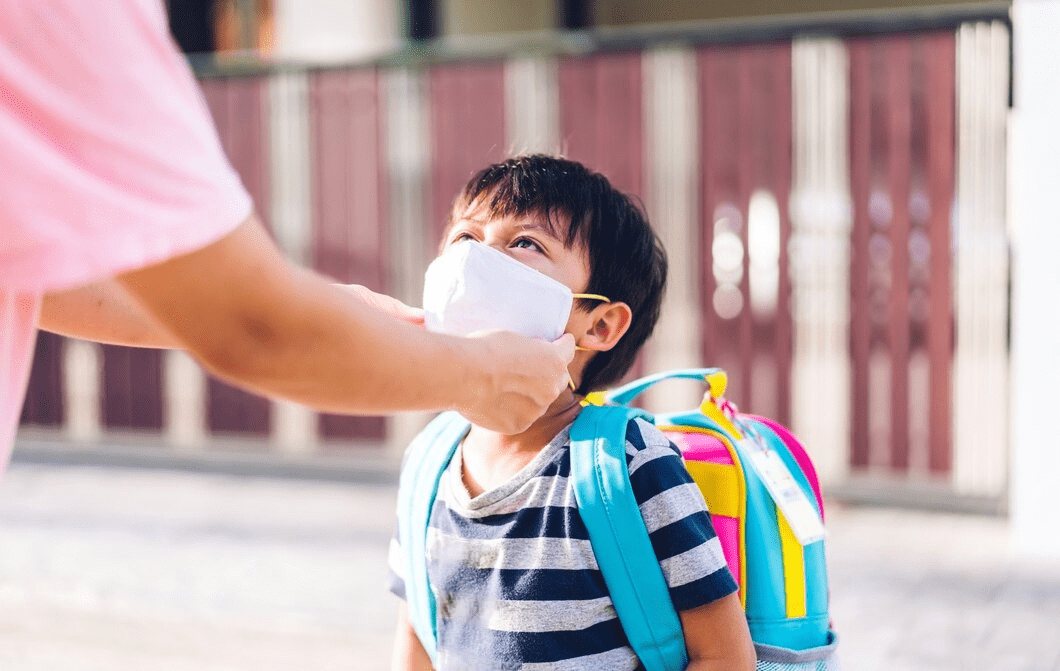Child with a colorful backpack standing in front of a gate.