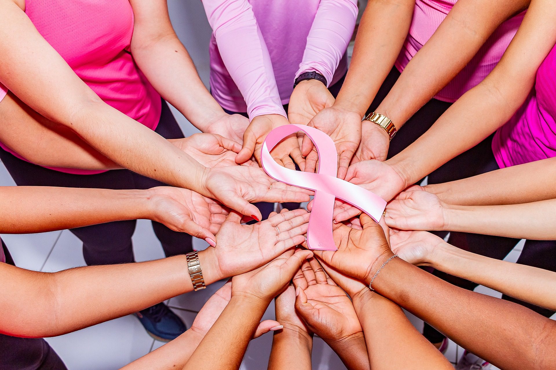 Hands together holding a pink ribbon for breast cancer awareness.